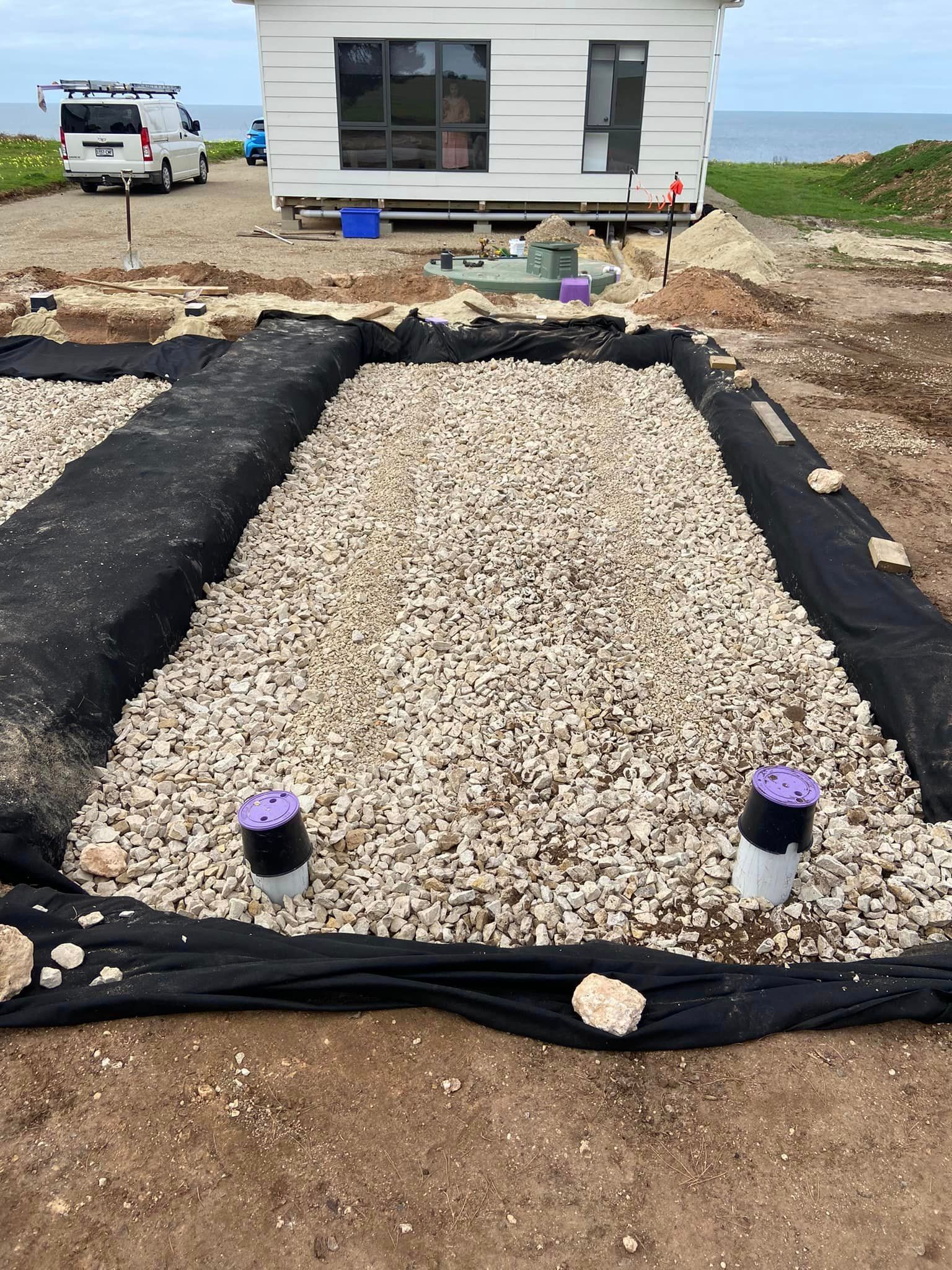 A gravel area in front of a house with a van parked in the background.