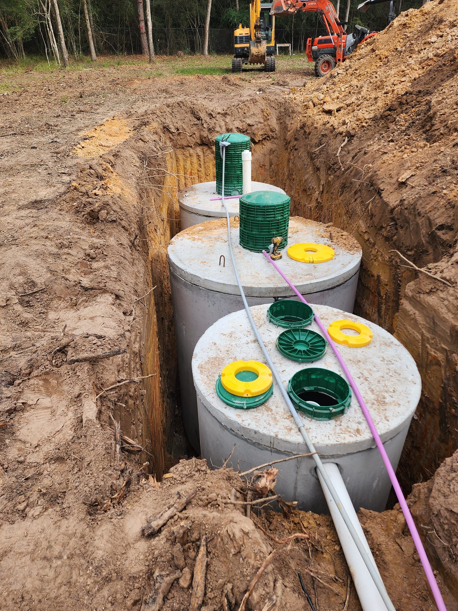 A row of septic tanks are being installed in a dirt field.