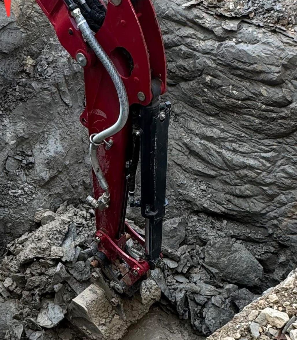 A red excavator is digging a hole in the ground