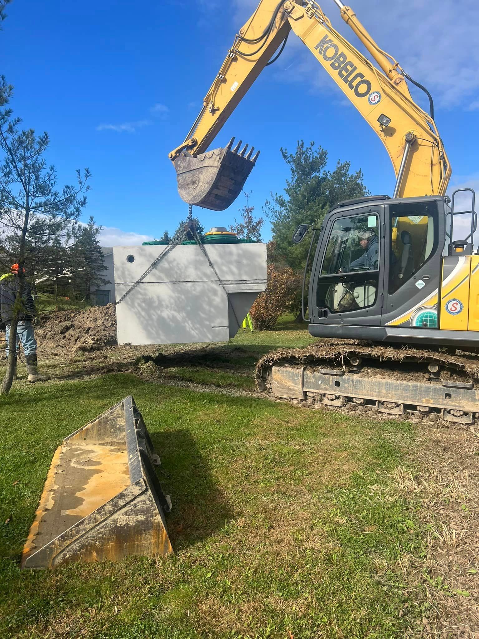 A yellow excavator is digging a hole in the grass.