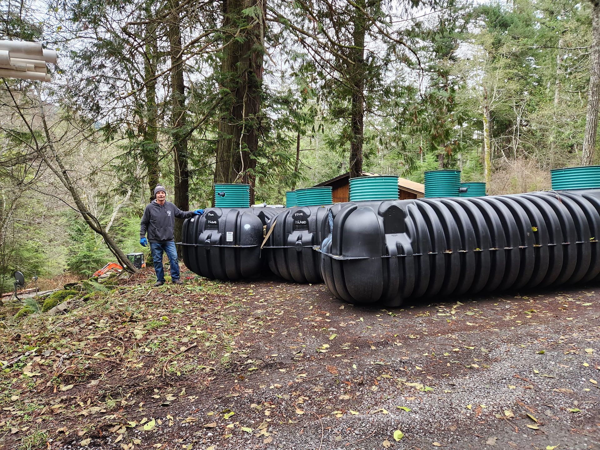 A man is standing next to a large black tank in the middle of a forest.