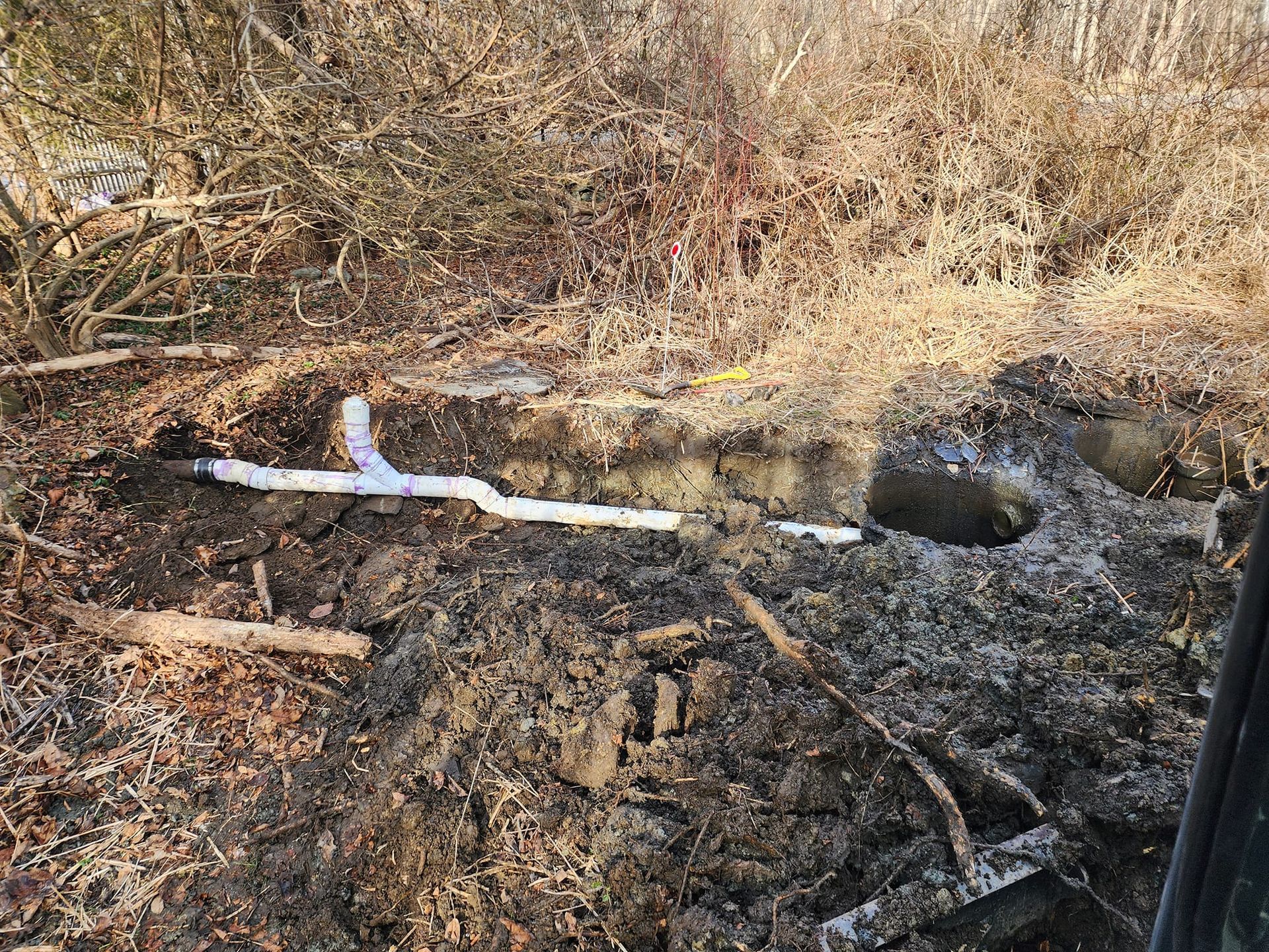 A pipe is laying in the dirt next to a hole in the ground.