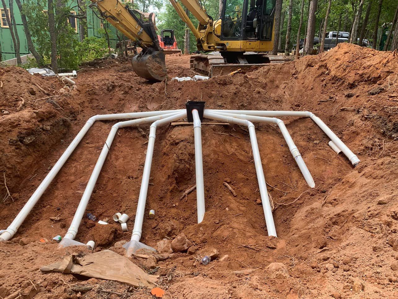 A yellow excavator is digging a hole in the dirt with pipes in it.