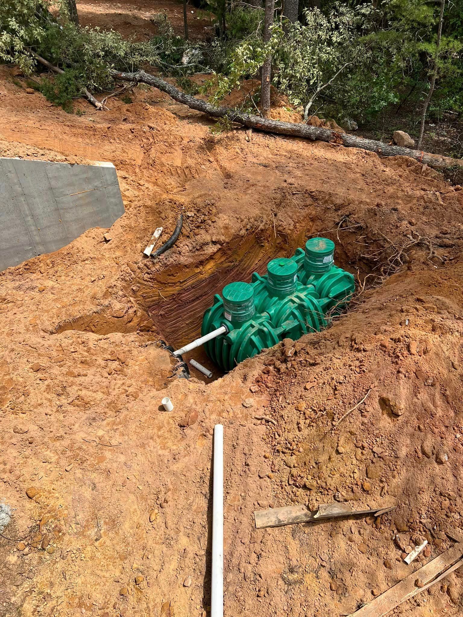 A green septic tank is sitting in a hole in the dirt.