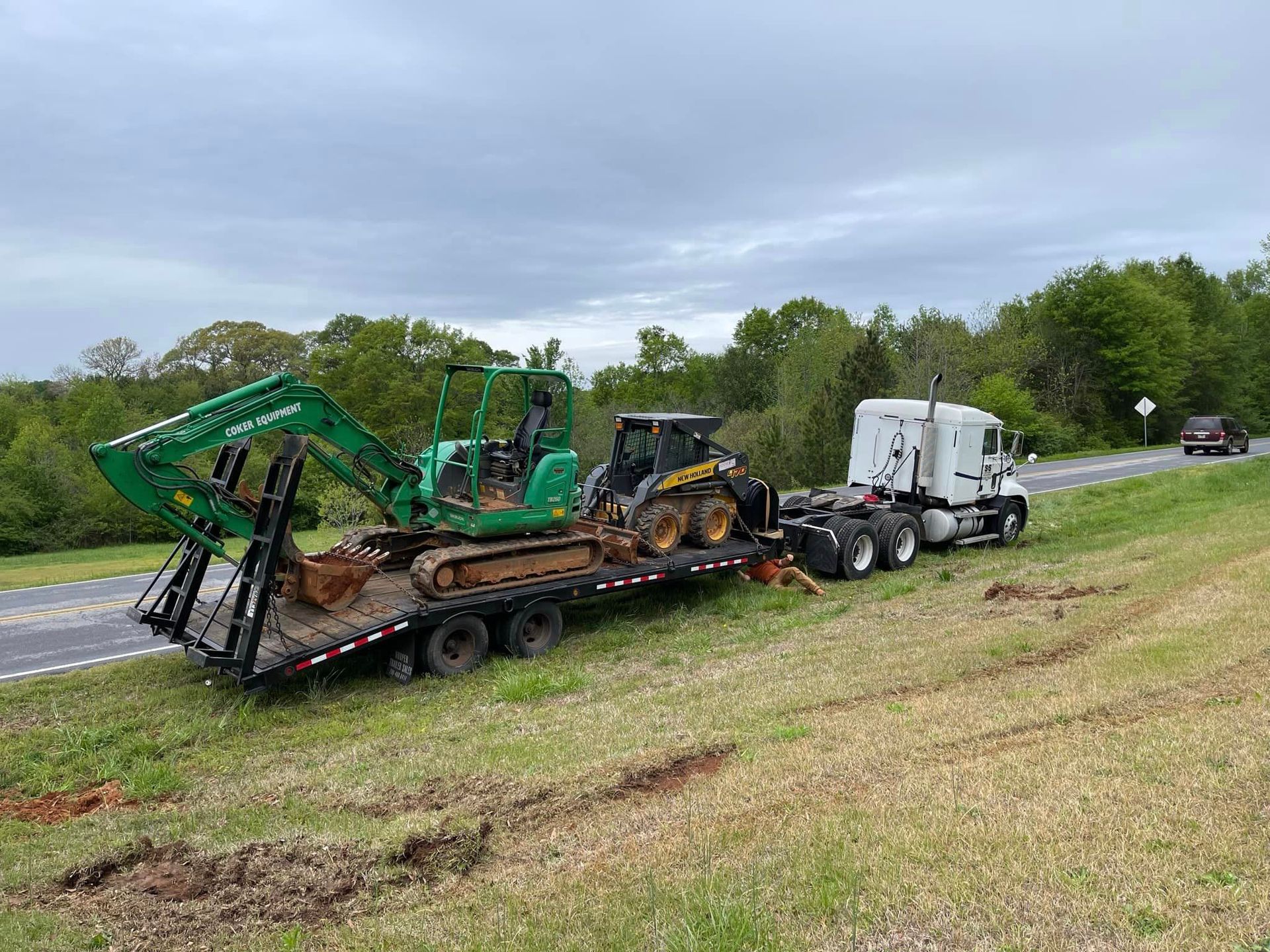 A truck is carrying a green excavator on a trailer.