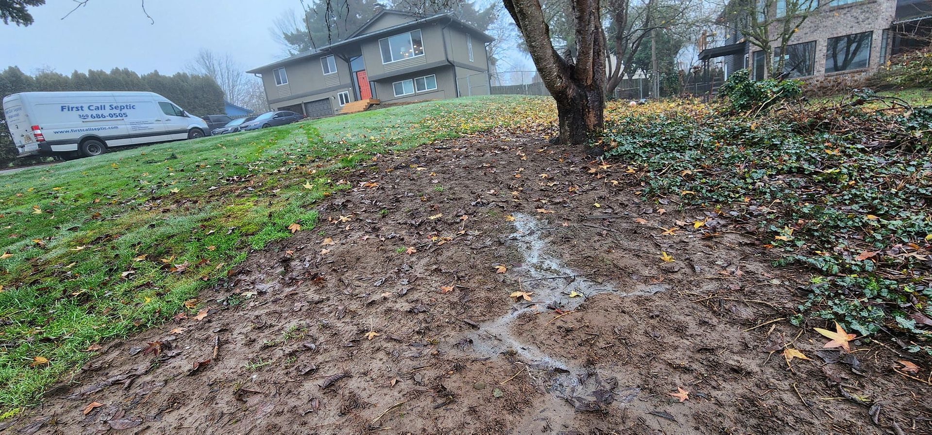 A muddy field with a white van parked in the background and a house in the background.