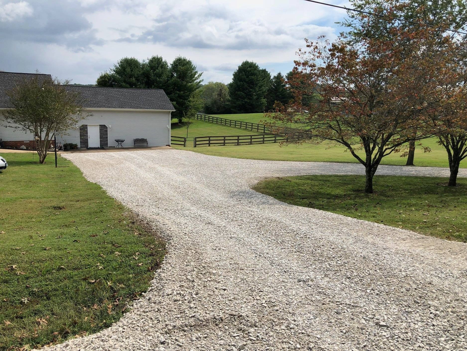 A gravel driveway leading to a house with a barn in the background.