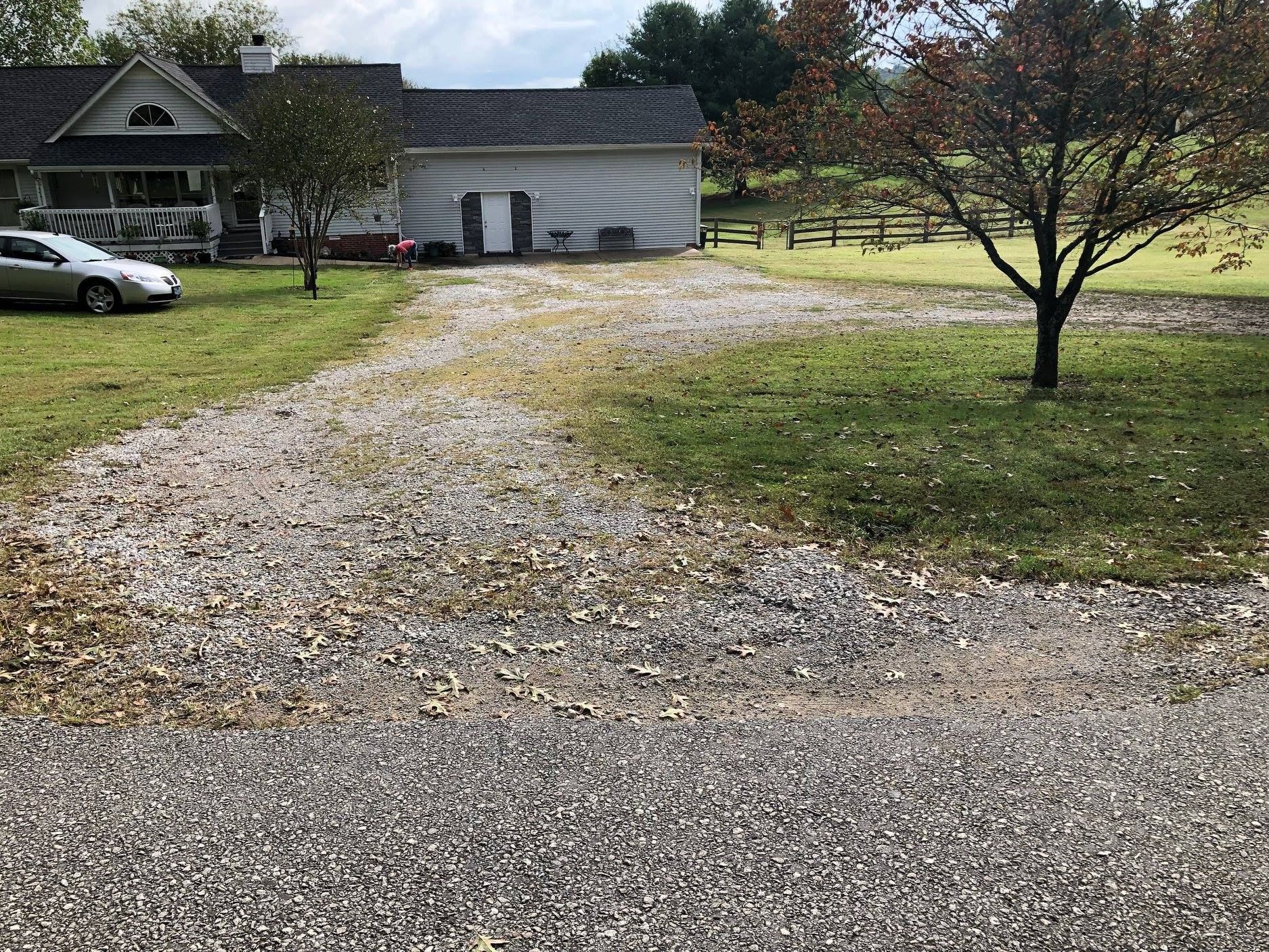 A gravel driveway leading to a house with a car parked in front of it.