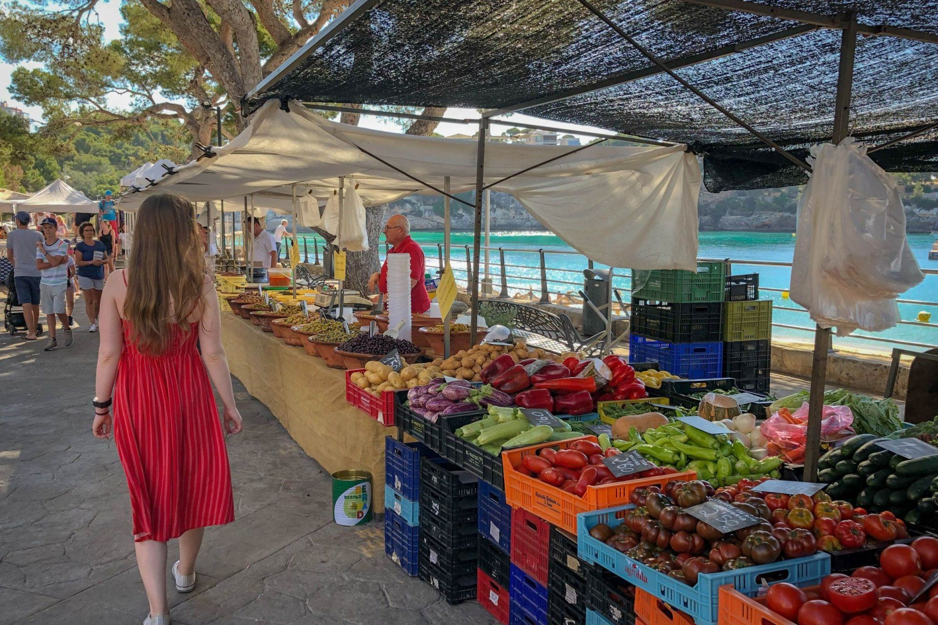 a woman in a red dress walks past a fruit and vegetable stand