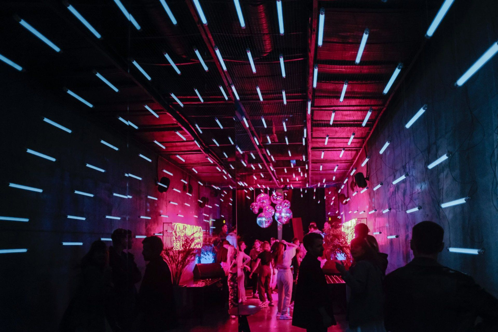 a group of people are standing in a dark room with neon lights hanging from the ceiling