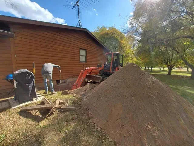 a man is digging a hole in front of a house with an excavator .