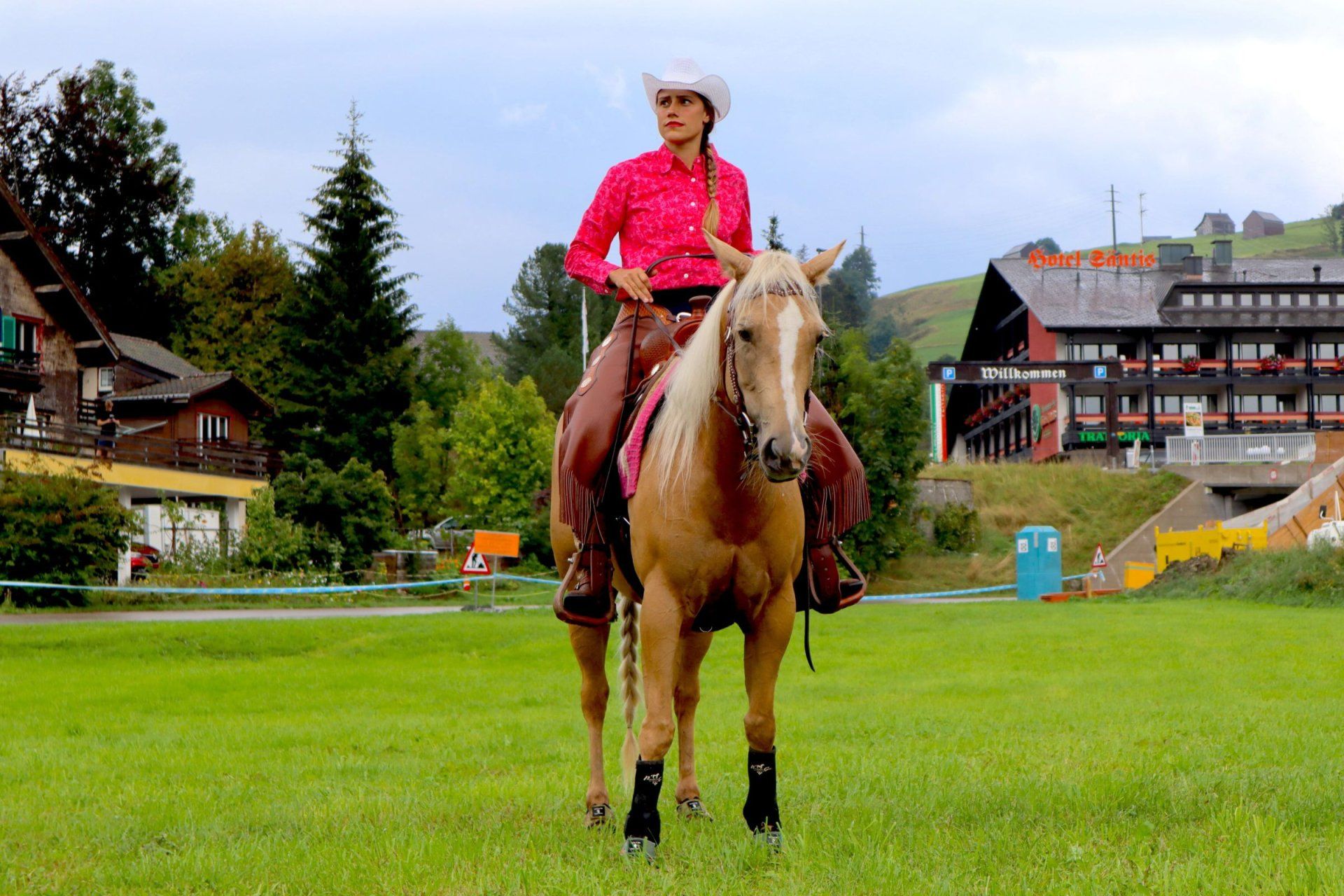a woman riding a horse in a field with a hotel in the background