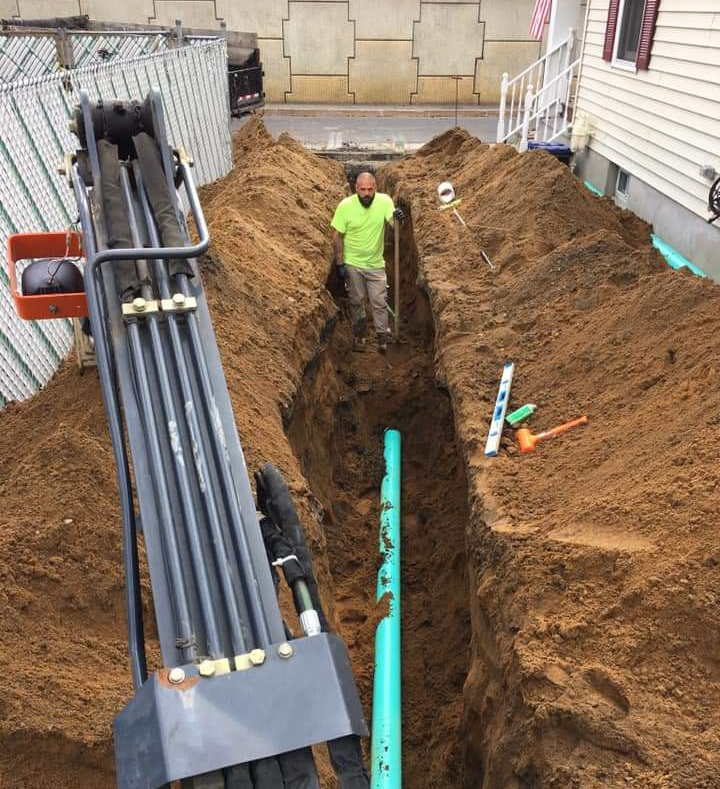 a man in a green shirt is digging a hole for a pipe