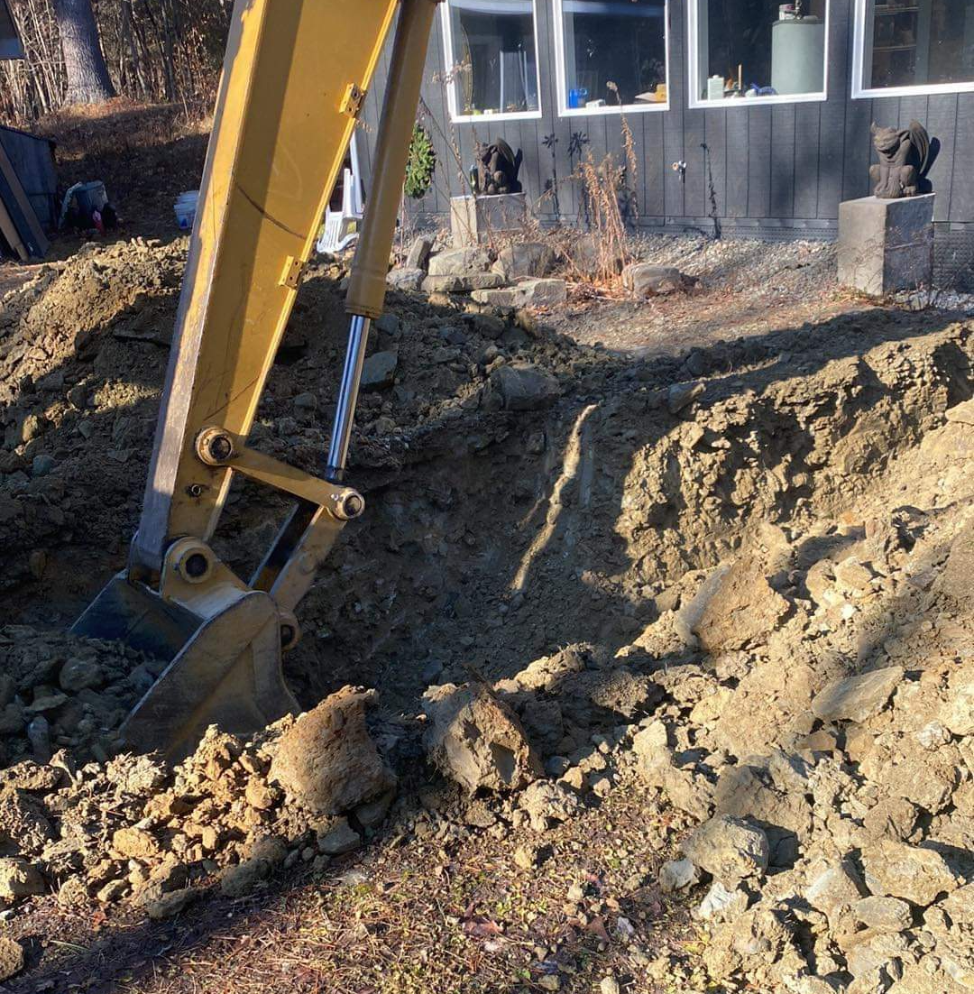 a yellow excavator is digging a hole in the dirt in front of a house