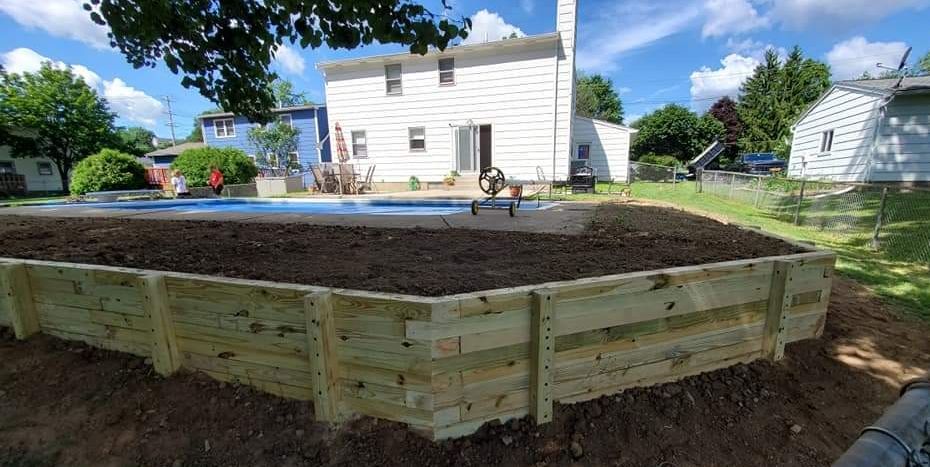 A wooden fence is surrounding a large pile of dirt in front of a house.