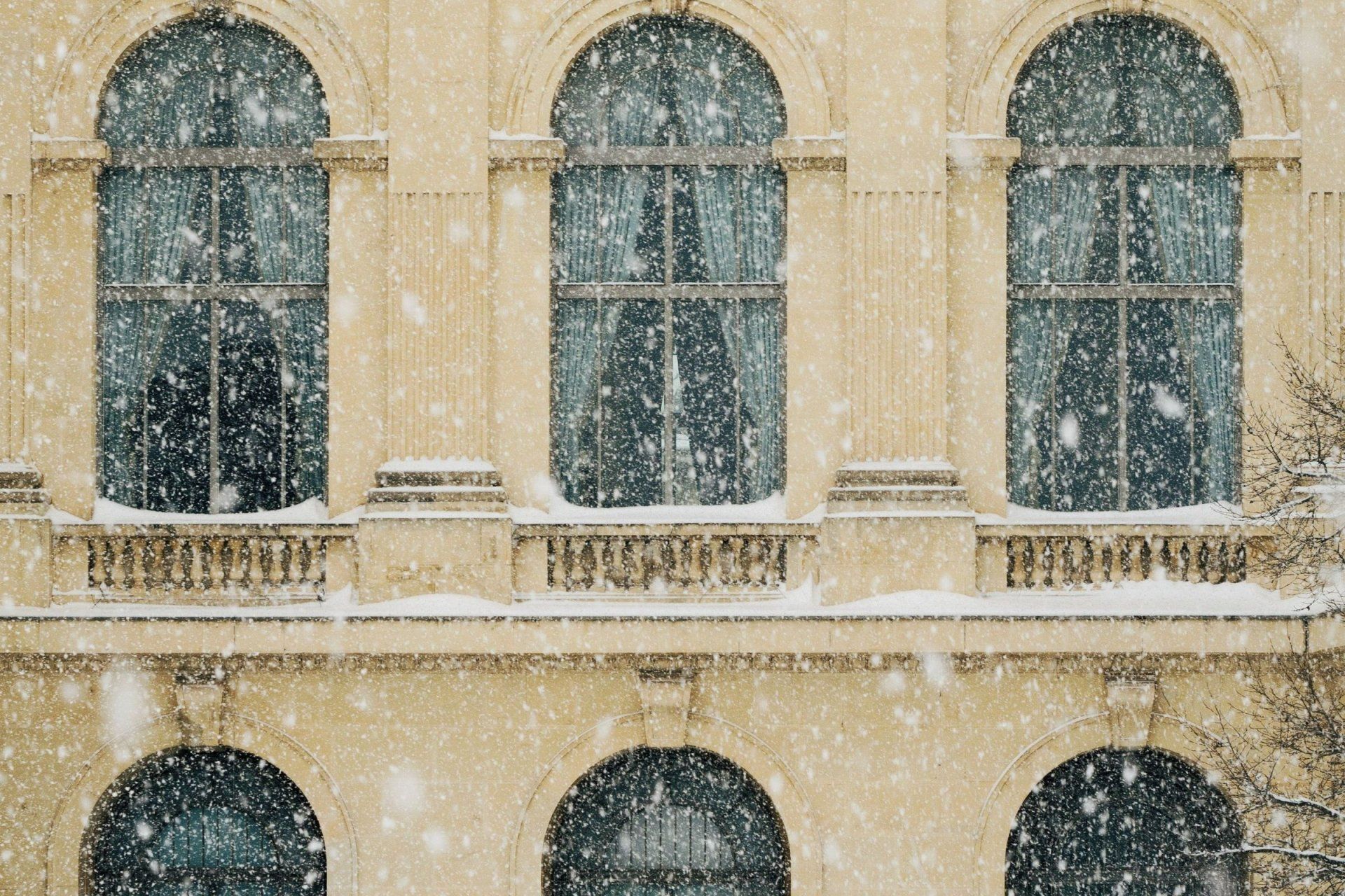 snow is falling on a building with arched windows