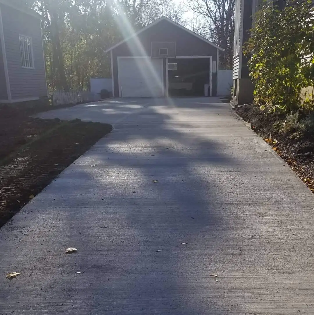 a driveway leading to a garage with the sun shining through the trees