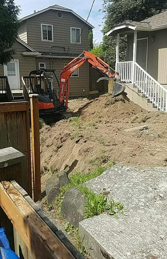 An excavator is digging a hole in the backyard of a house.