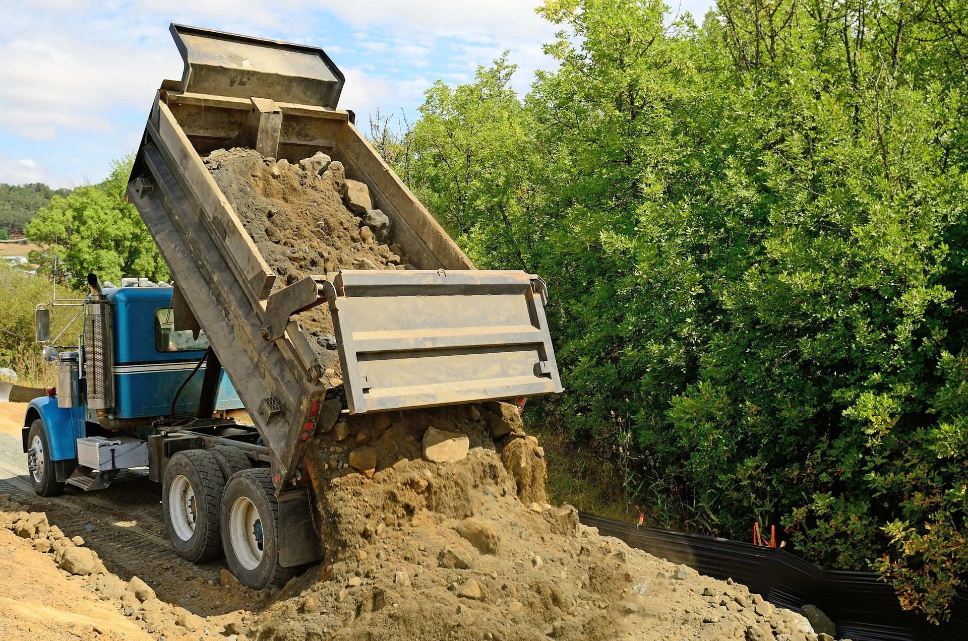 A dump truck is dumping dirt on a dirt road.