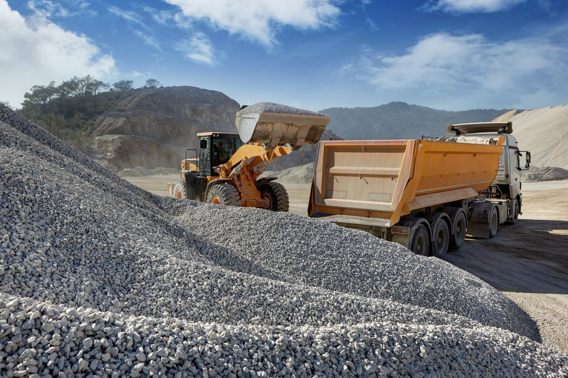 A dump truck is being loaded with gravel at a construction site.