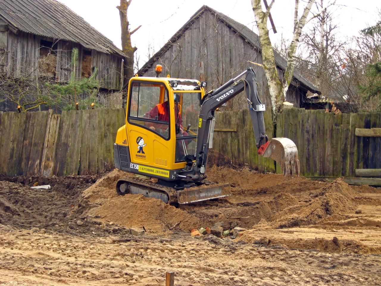 A yellow excavator is digging a hole in a dirt field.