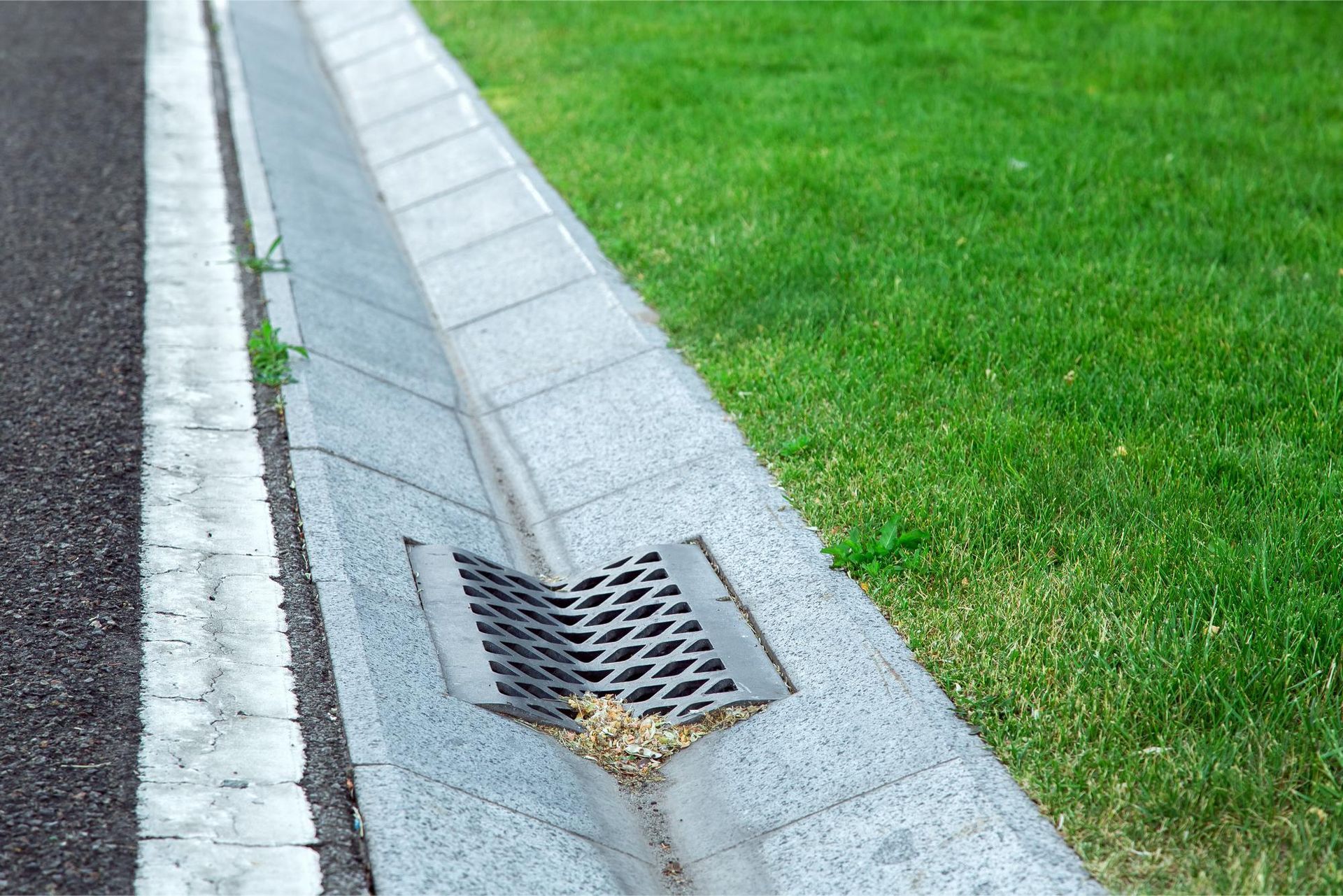 A drain on the side of a road next to a grassy area.