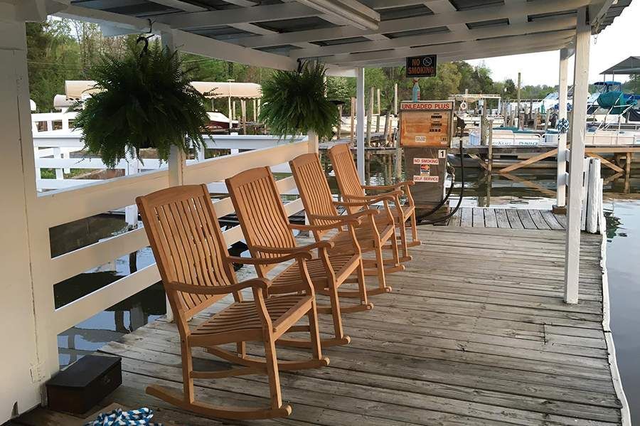 A row of wooden rocking chairs on a dock overlooking a body of water.