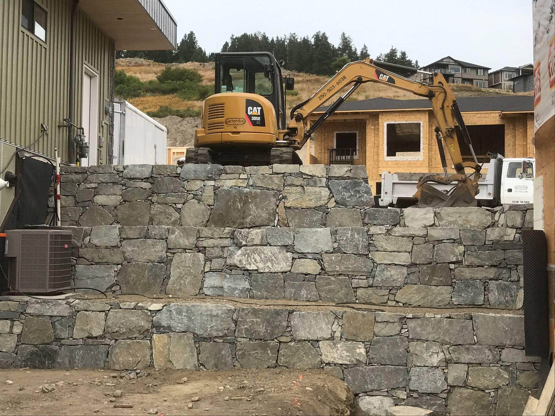 A cat excavator is sitting on top of a stone wall.