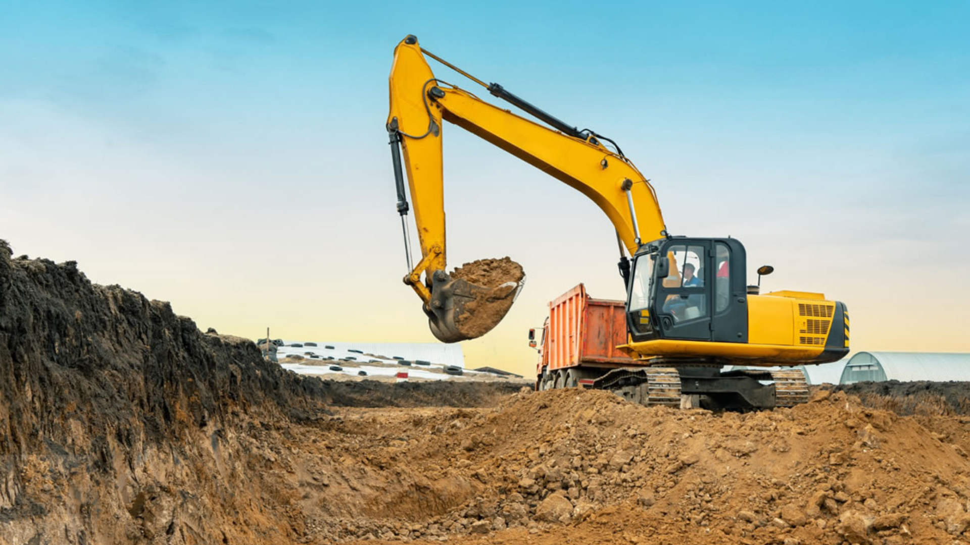 A yellow excavator is digging a hole in a dirt field.