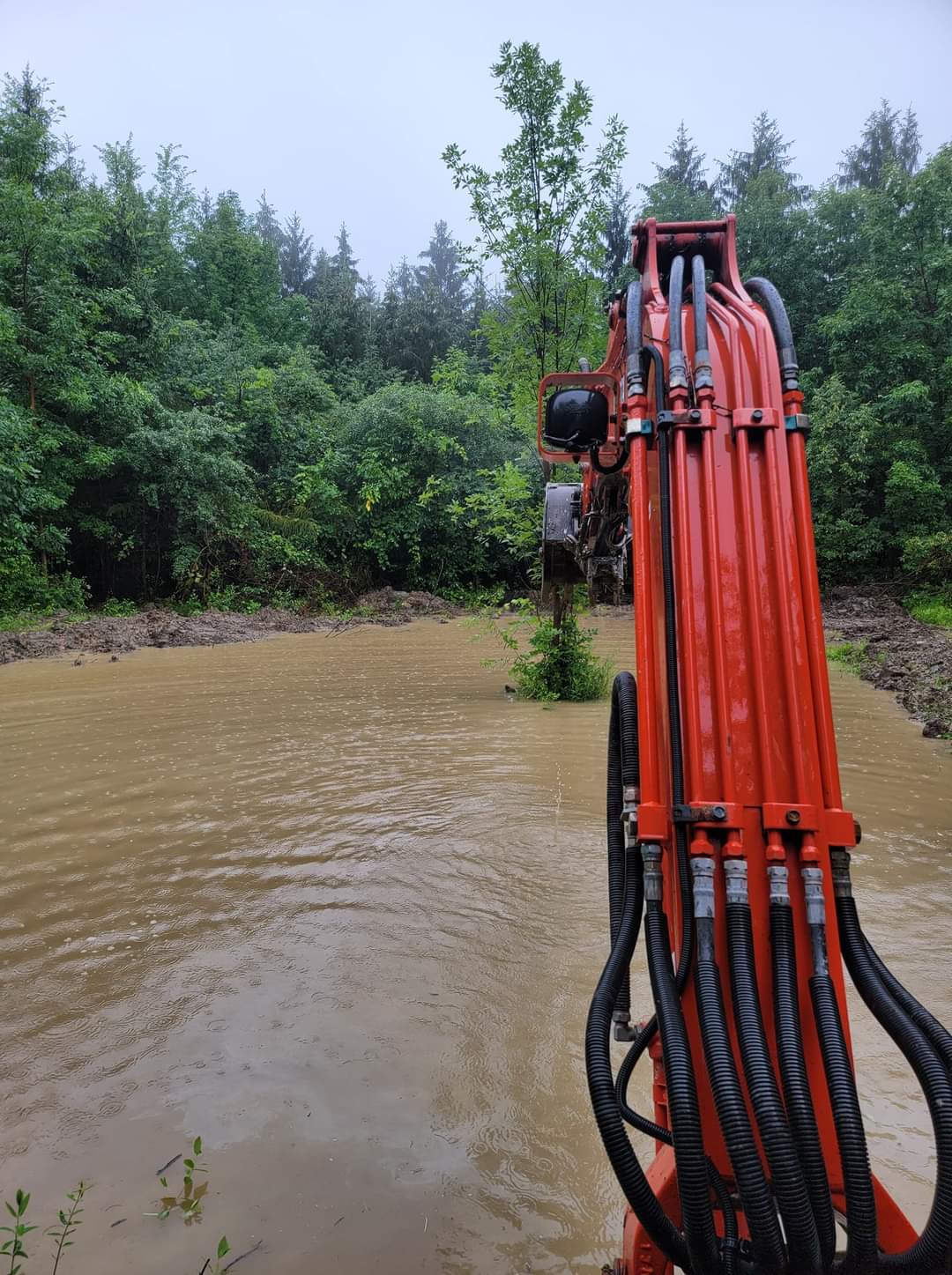 a red excavator is in a flooded area with trees in the background