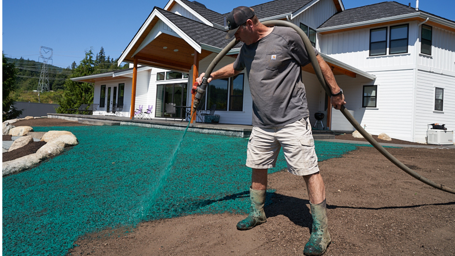 A man is spraying a lawn with a hose in front of a house.