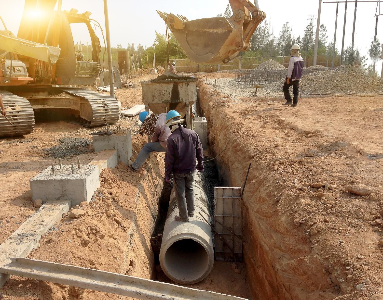 a group of construction workers are working on a pipe in a trench .