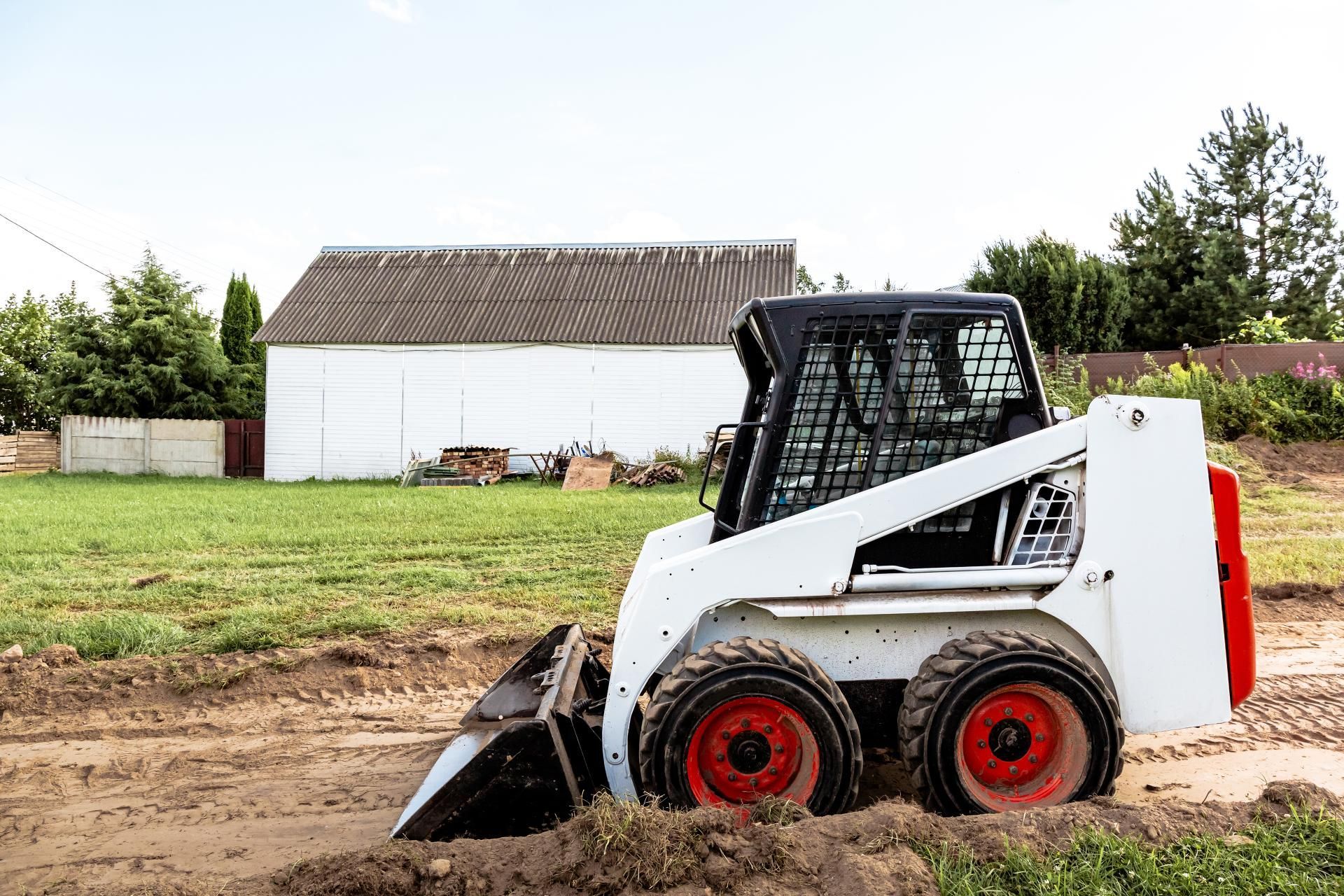 a bulldozer is moving dirt in front of a white barn