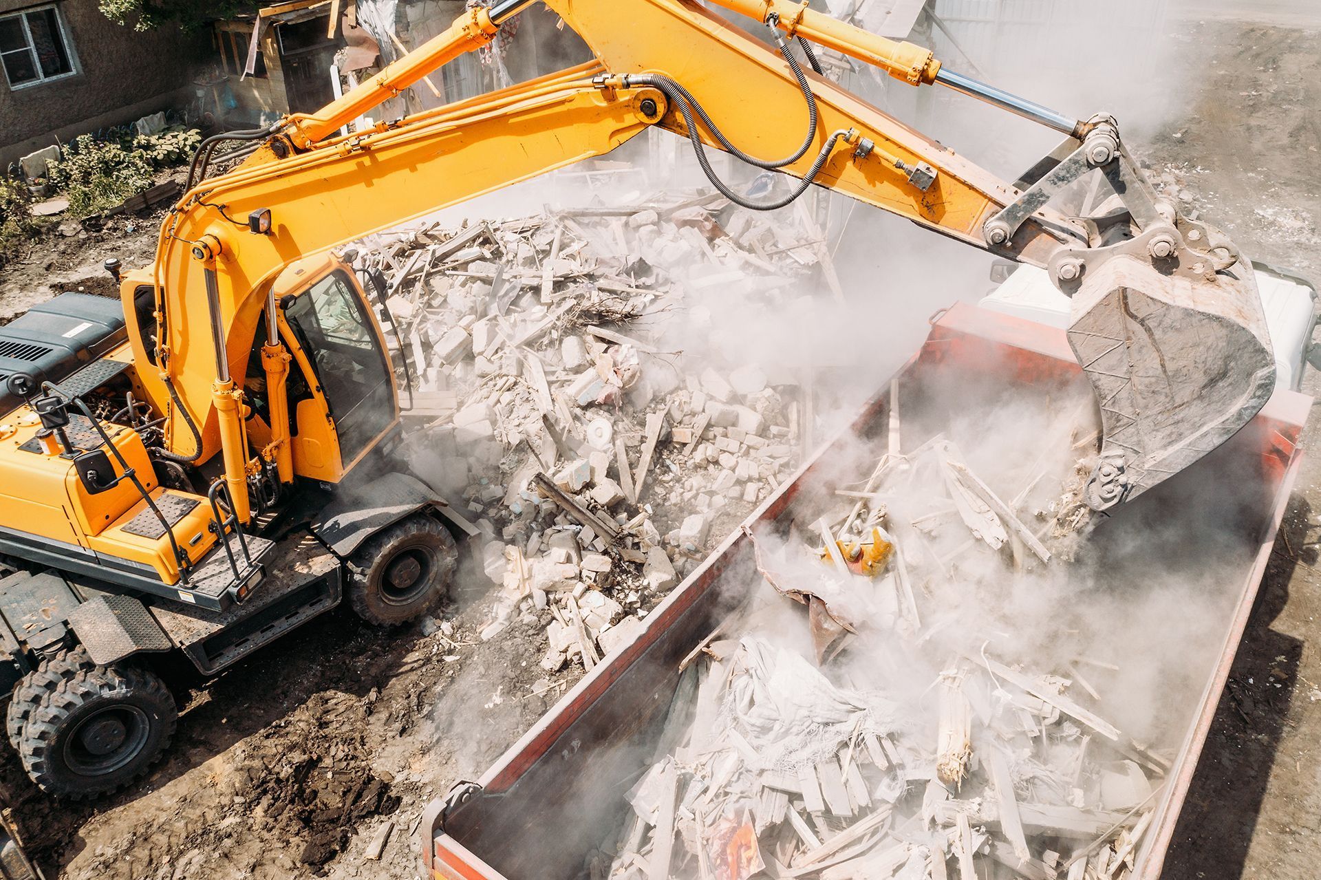 a yellow excavator is loading rubble into a dumpster