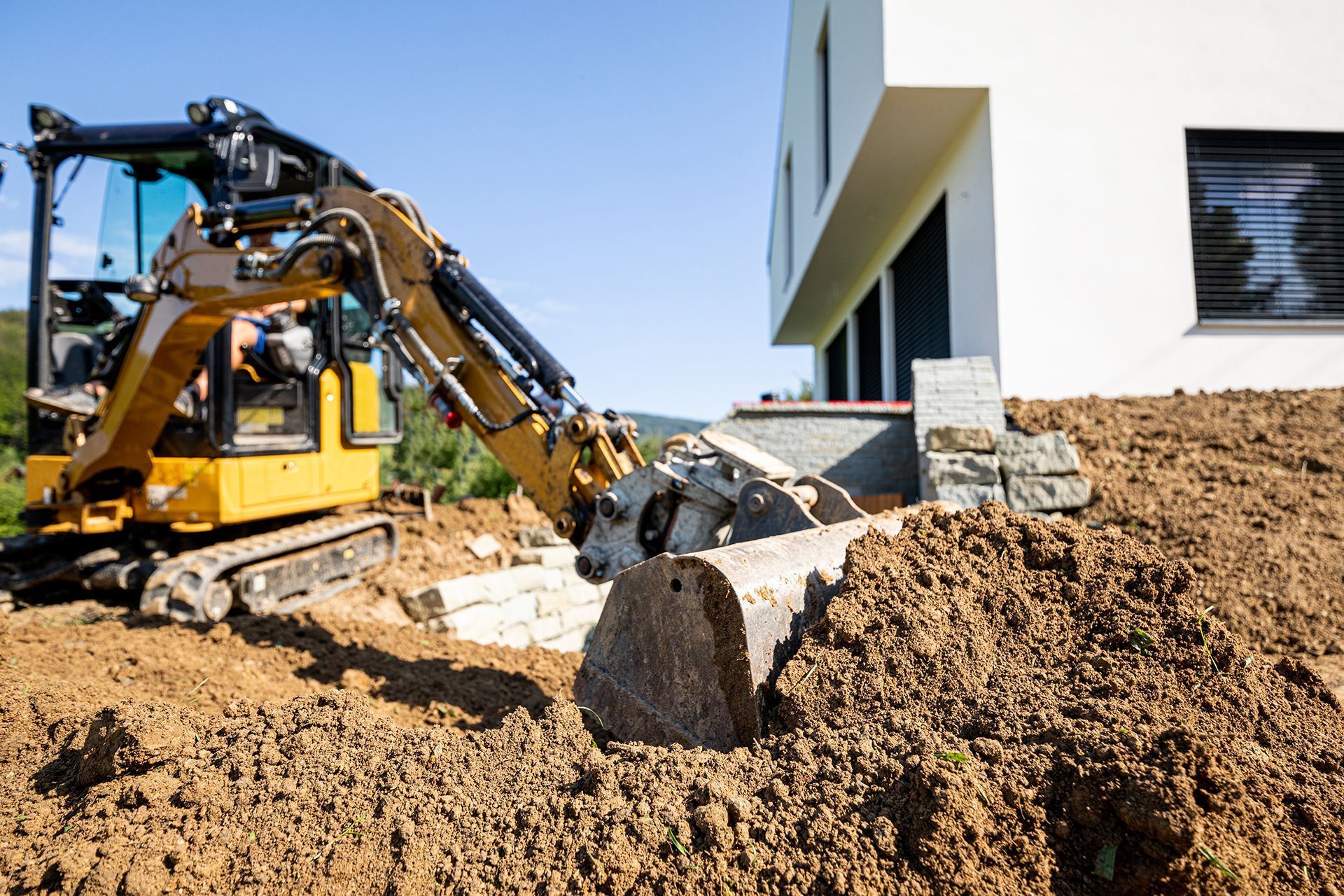 a yellow excavator is moving dirt in front of a house