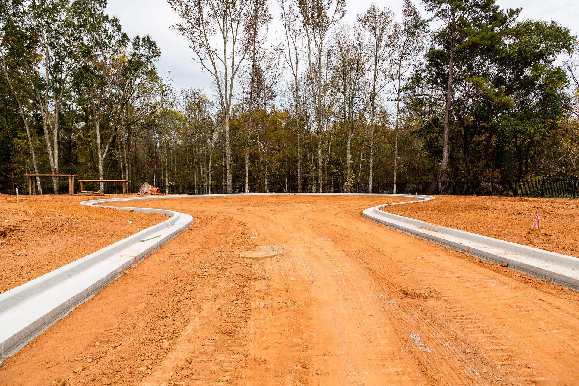 A dirt road with a curb and trees in the background.