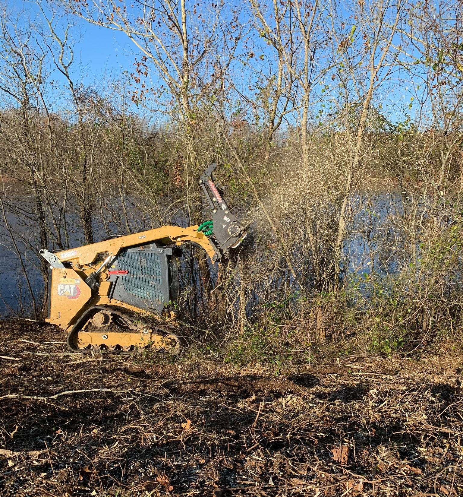 a cat tractor is clearing brush near a body of water