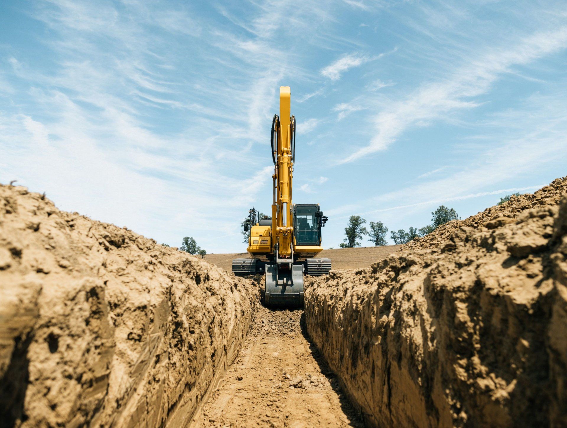 a yellow excavator is digging a trench in the dirt