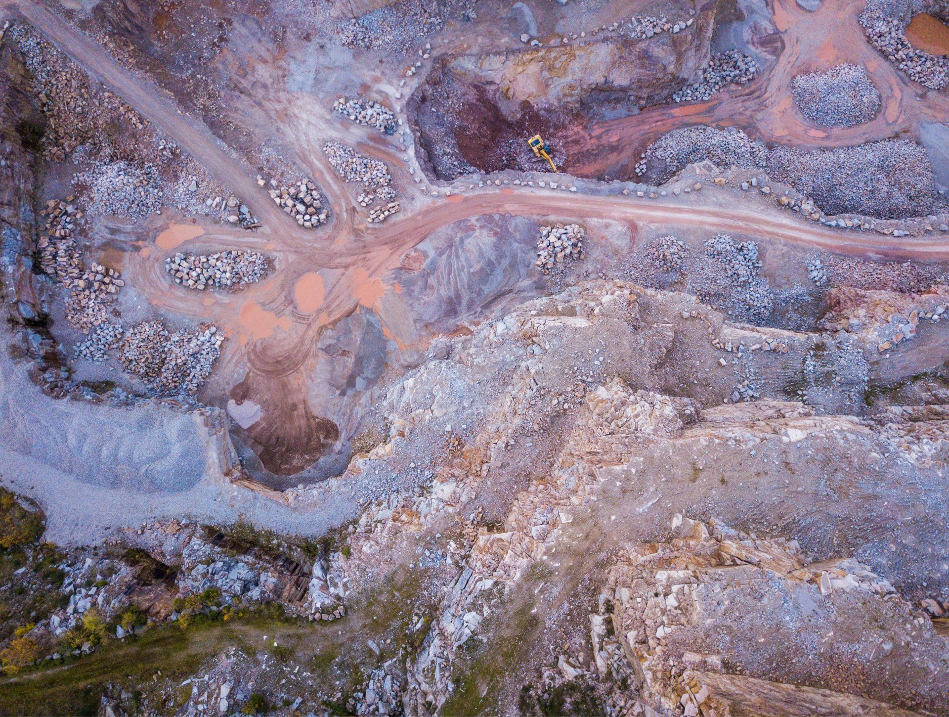 an aerial view of a rocky area with a yellow excavator in the middle