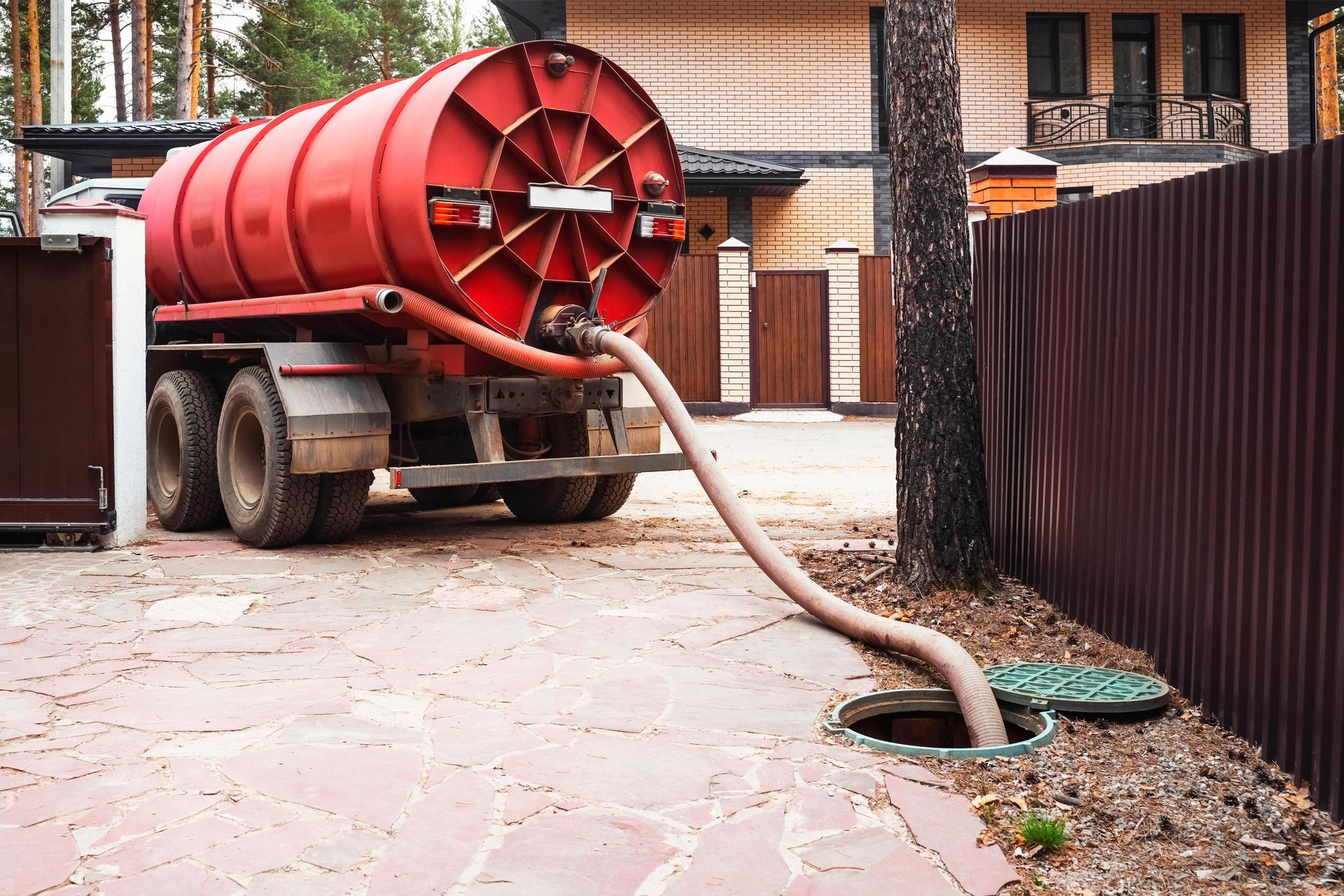 A red vacuum truck is pumping water into a septic tank.