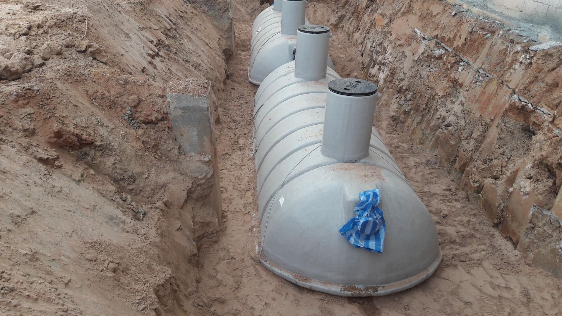 A row of septic tanks are sitting in a dirt trench.