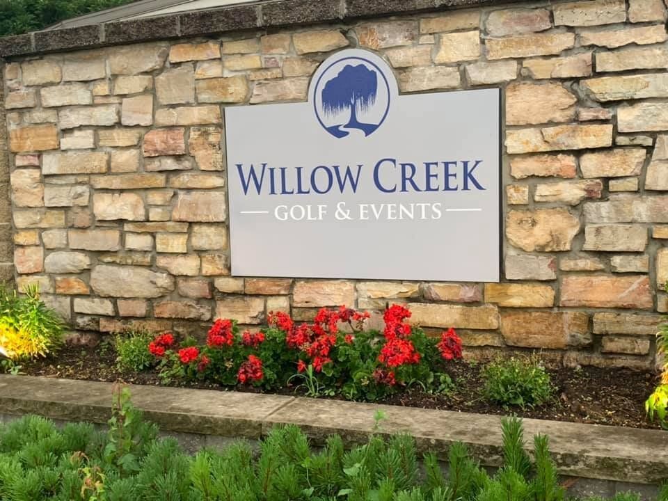 A sign for willow creek golf and events is on a stone wall.