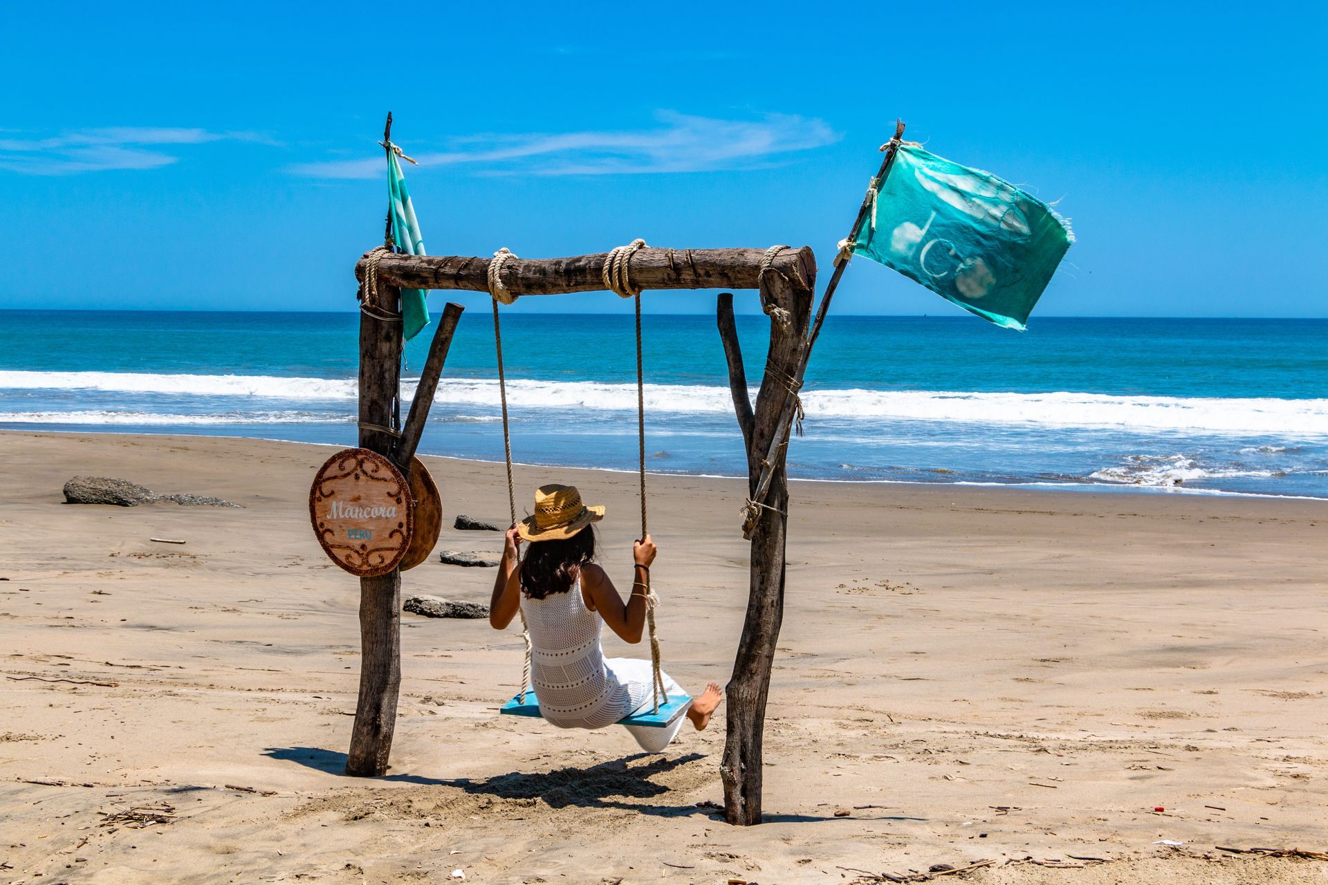 A woman is sitting on a wooden swing on the beach.
