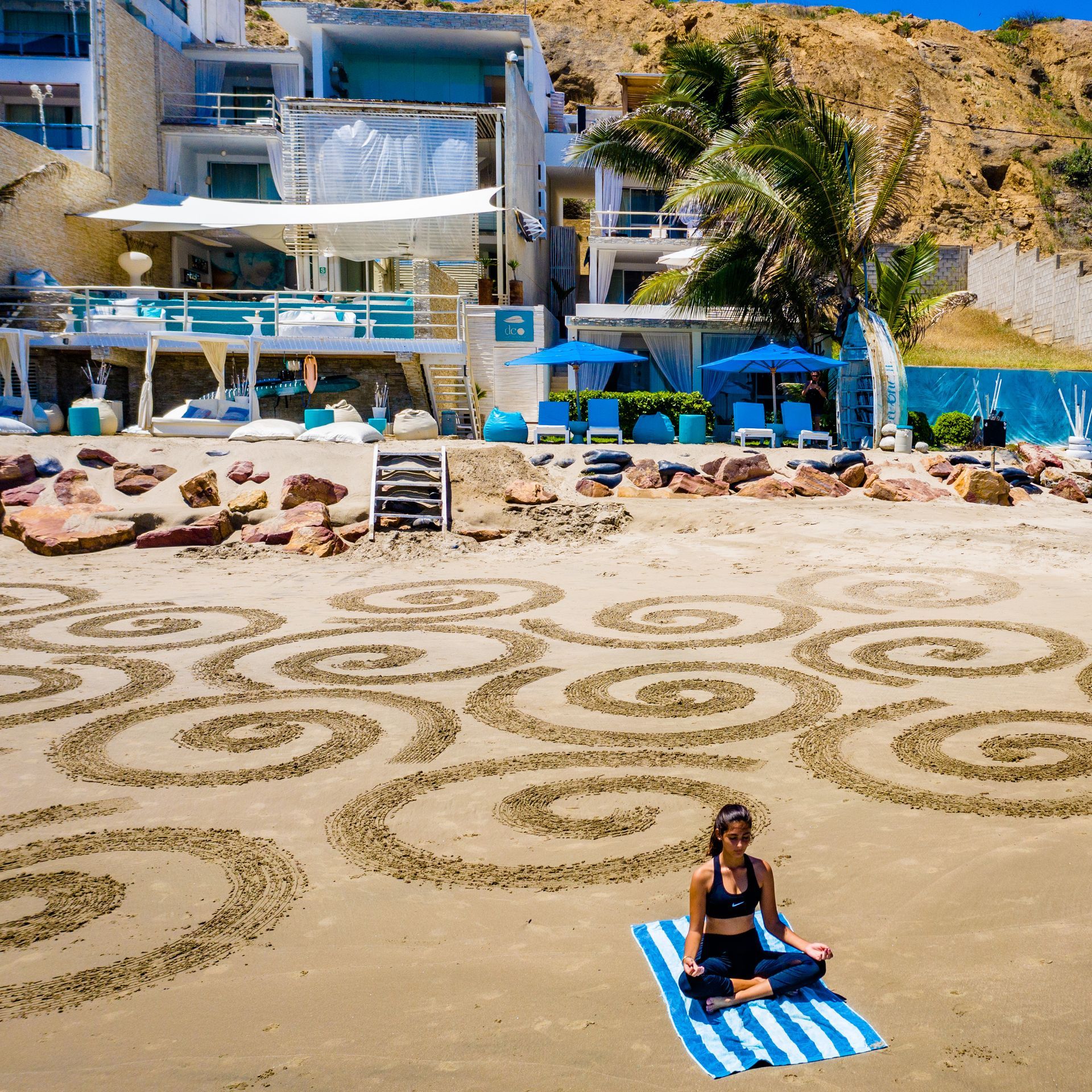 A woman is sitting in a lotus position on a towel on the beach.