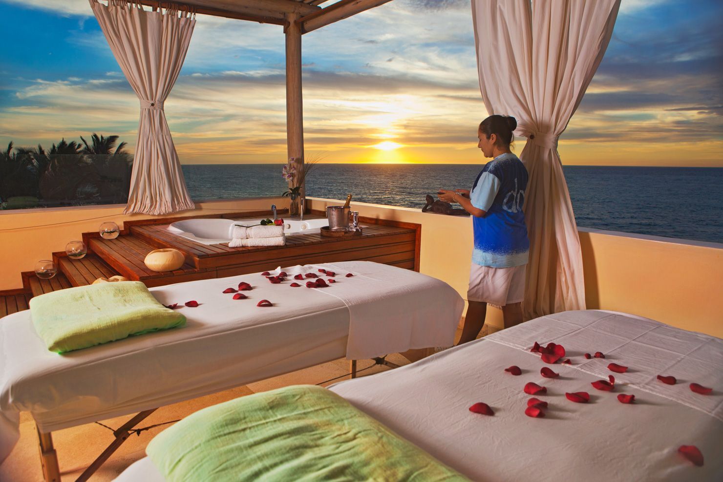 A woman is standing in front of two massage tables with roses on them.