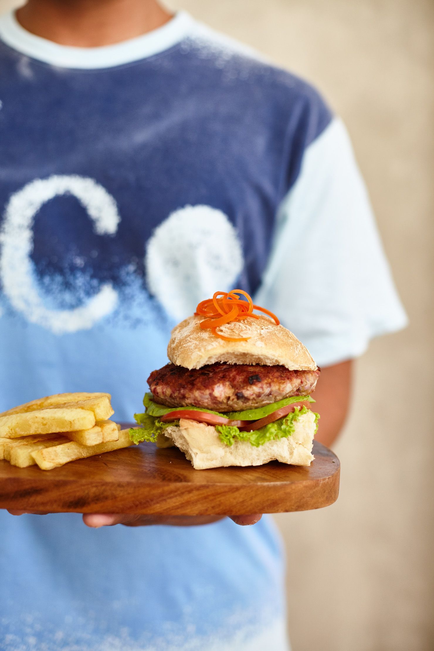 A person is holding a wooden cutting board with a hamburger and french fries on it.