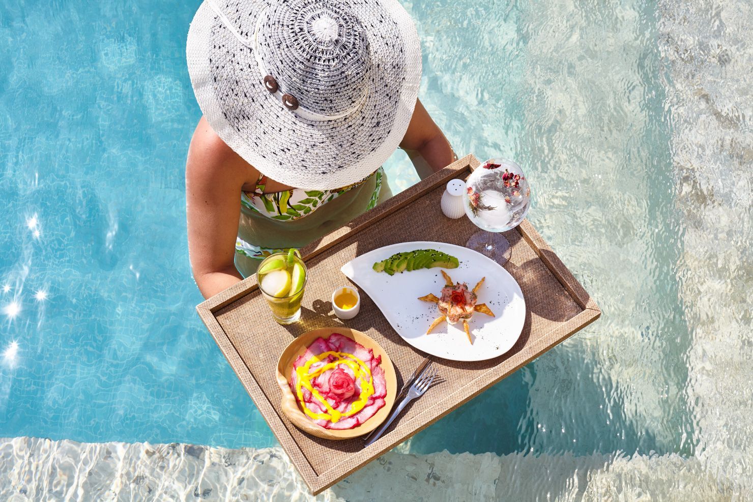 A woman is holding a tray of food in a swimming pool.
