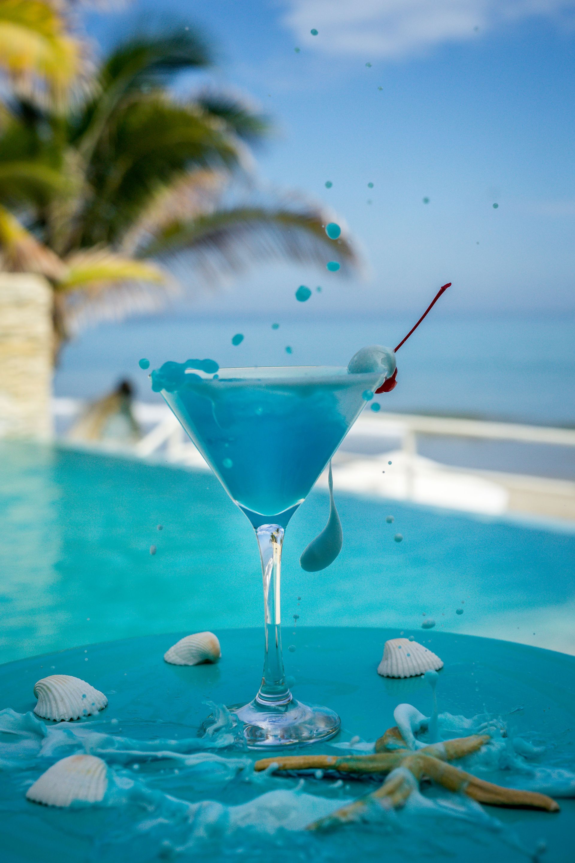 A blue martini is sitting on a table next to a swimming pool.