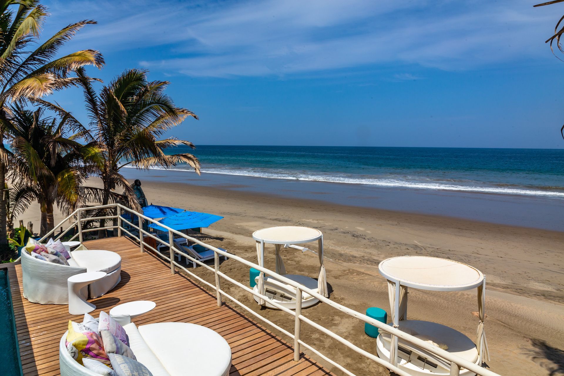 A wooden deck overlooking a beach with tables and chairs.