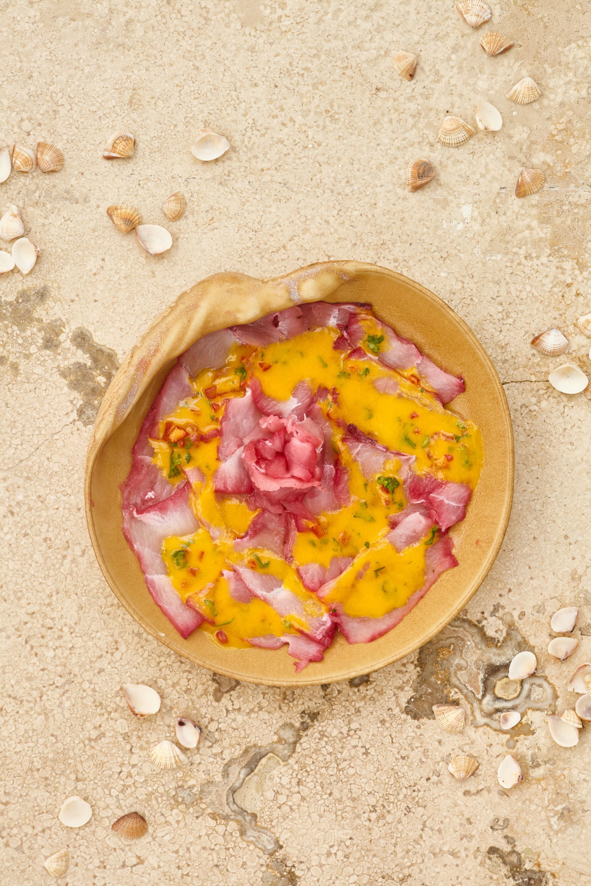 A wooden bowl filled with food is sitting on a sandy beach.